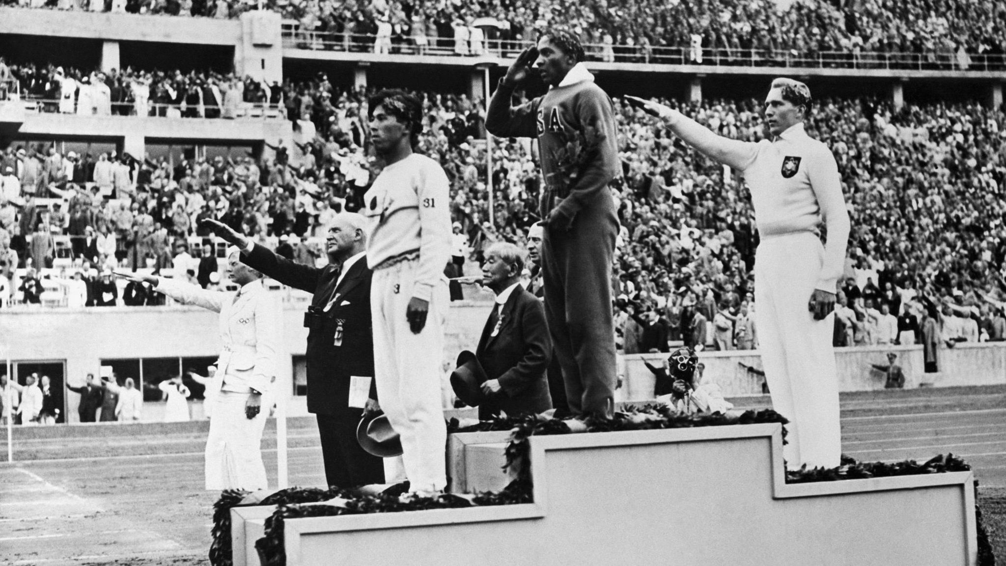 Jesse Owens on top of the podium after winning long jump gold at the 1936 Olympics in Berlin, alongside Germany's Luz Long (silver) and Japan's Naoto Tajima (bronze)