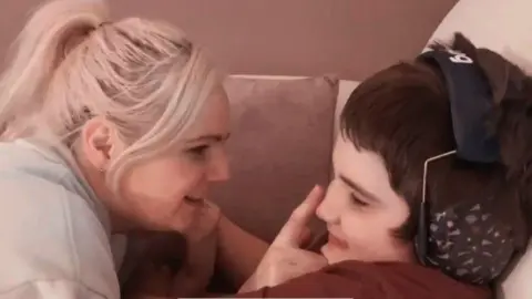 Family Charlotte looks at her son with a smile Tobie while touching his nose with her finger. Tobie is smiling, he is wearing a set of ear defenders