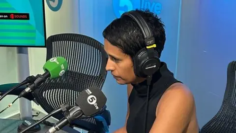 Naga Munchetty wearing headphones talking into 5Live microphone in a studio