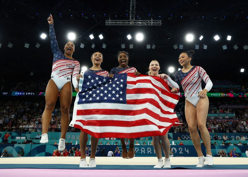 © Reuters. Paris 2024 Olympics - Artistic Gymnastics - Women's Team Final - Bercy Arena, Paris, France - July 30, 2024. Simone Biles of United States, Jordan Chiles of United States, Jade Carey of United States, Sunisa Lee of United States and Hezly Rivera of United States celebrate with their national flag after winning gold. REUTERS/Hannah Mckay 