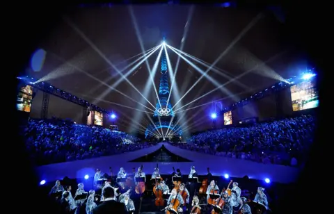  Paweł Kopczyński/Reuters The Eiffel Tower is illuminated with lights and lasers and the Olympic sign with an orchestra in foreground, during the opening ceremony of the Paris 2024 Olympics.