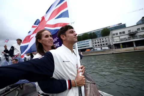  Naomi Baker/Reuters Flagbearers Tom Daley and Helen Glover, of Team GB, gesture on a boat while holding the national flag on the River Seine during the opening ceremony