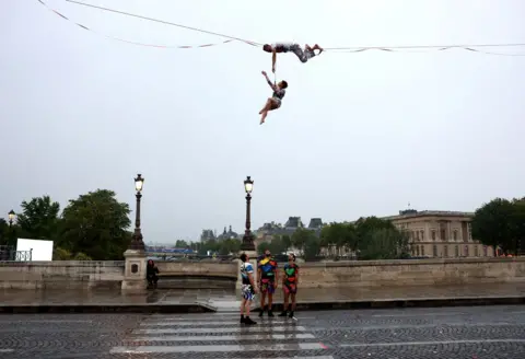  Maddie Meyer/Getty Images Tightrope walker Nathan Paulin performs on a high rope during the athletes’ parade on the River Seine near the Supreme Court during the opening ceremony of the Olympic Games Paris 2024