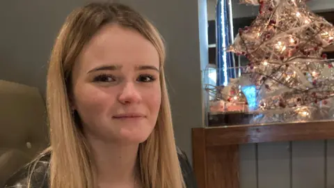 Family handout Amelia Butlin with blonde hair, gazing at the camera with a small faux Christmas tree in the background. 