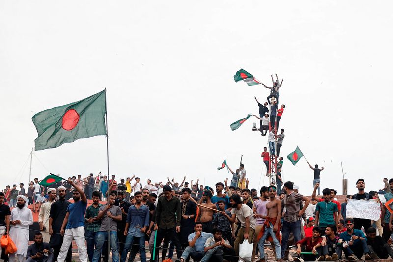 © Reuters. FILE PHOTO: People waves Bangladeshi flags on top the Ganabhaban, the Prime Minister's residence, as they celebrate the resignation of PM Sheikh Hasina in Dhaka, Bangladesh, August 5, 2024. REUTERS/Mohammad Ponir Hossain/File Photo