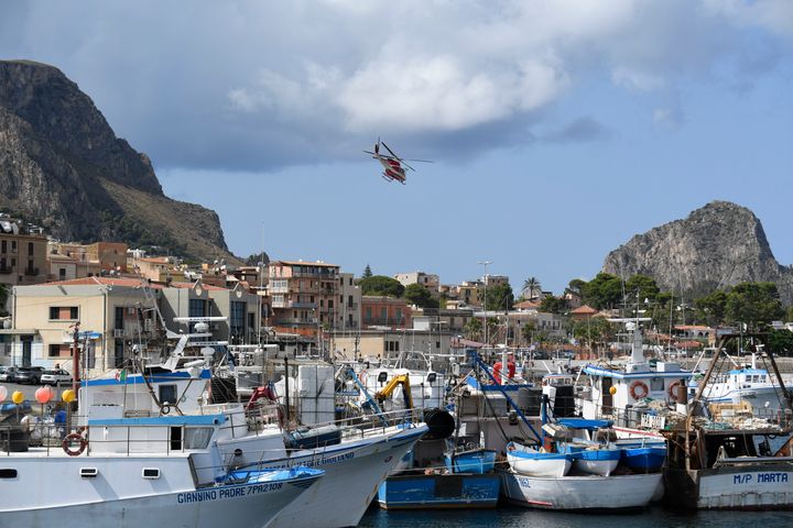 An Italian Firefighters helicopter flies over the harbor of Porticello, southern Italy, Tuesday, Aug. 20, 2024, as rescue teams and divers returned to the site of a storm-sunken superyacht to search for six people. (AP Photo/Salvatore Cavalli)