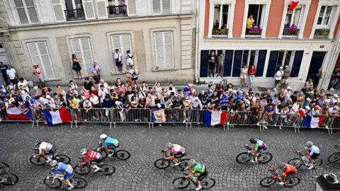 Getty Images People climb on window-ledges to watch cyclists during the Paris Olympics