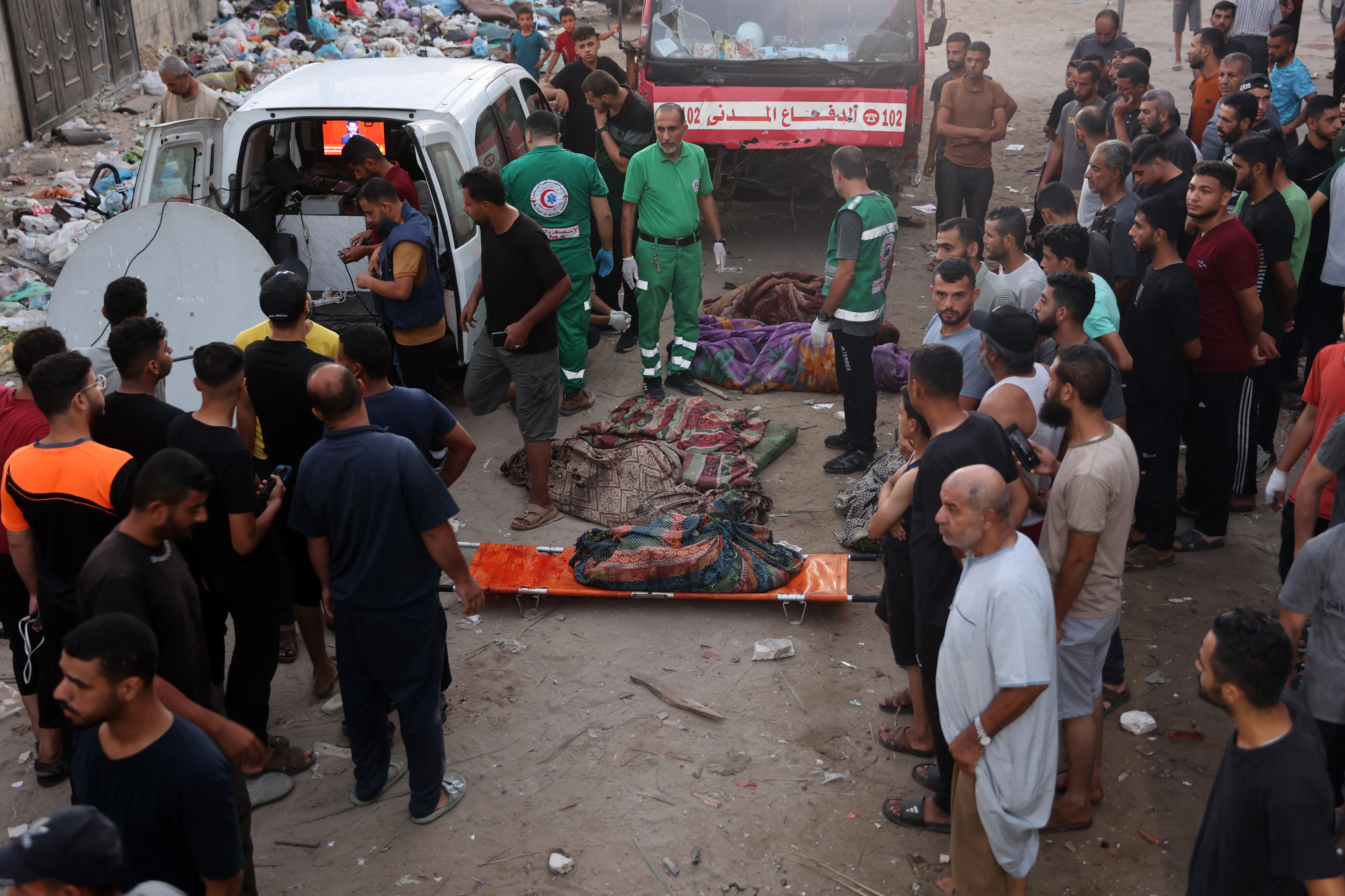 Onlookers watch as first responders prepare to transport bodies of Palestinians killed in an Israeli strike on a school in Gaza City on August 10, 2024, that killed dozens of people. (Photo by Omar AL-QATTAA / AFP) (Photo by OMAR AL-QATTAA/AFP via Getty Images)