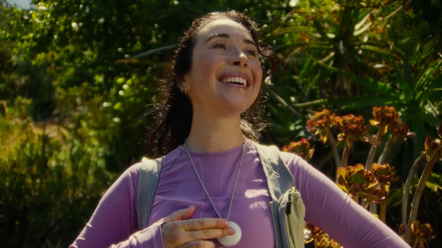 A young woman activates her "friend" AI necklace by pressing the center button