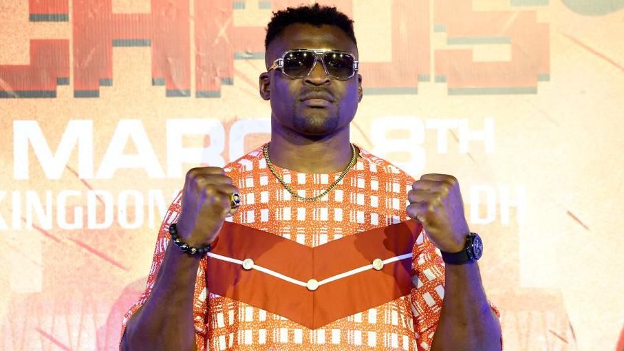 Francis Ngannou in sunglasses and with his fists in the air as he poses for pictures