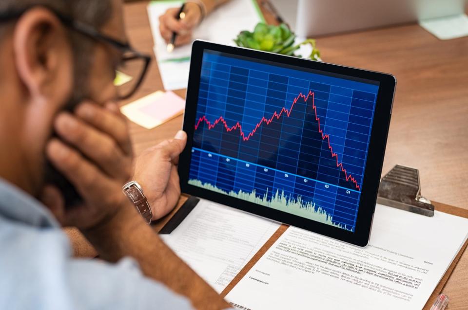 A visibly worried investor looking at a rapidly rising then plunging stock chart displayed on a tablet.