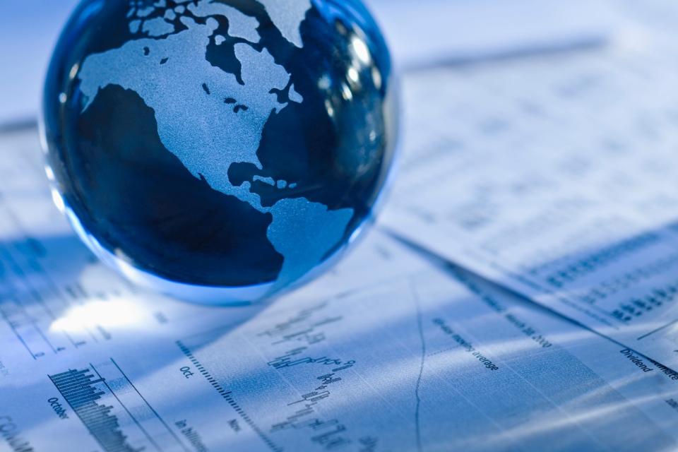 A marble-sized replica of the globe set atop financial paperwork displaying data and stock charts.