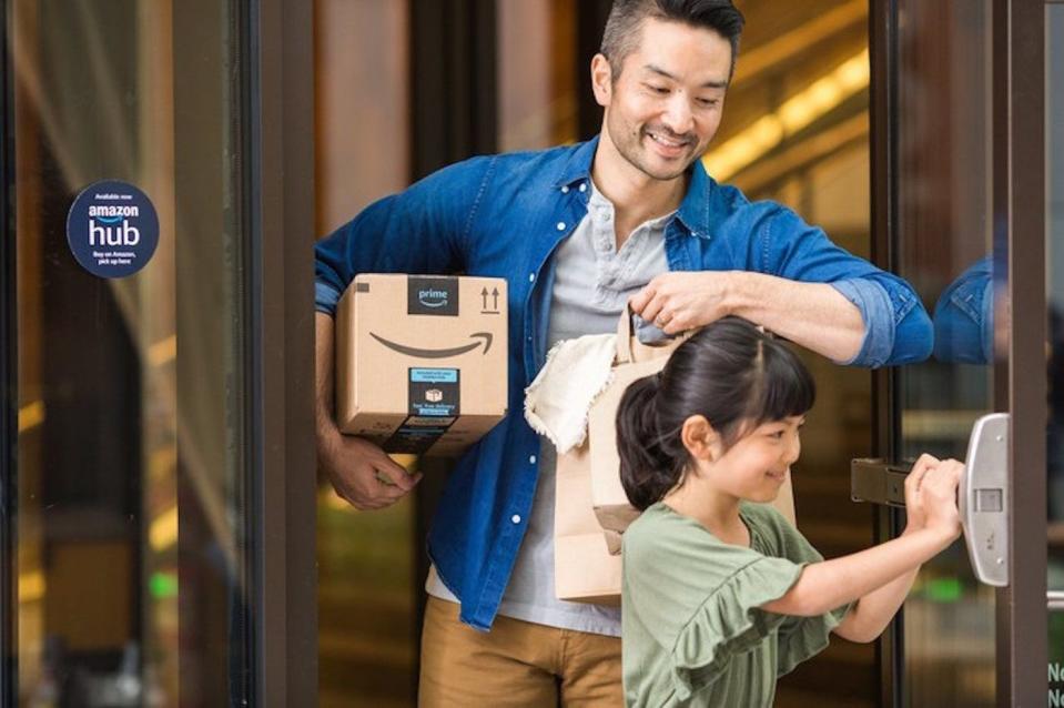 A parent carrying an Amazon package under their right arm while their child holds a door open for them.