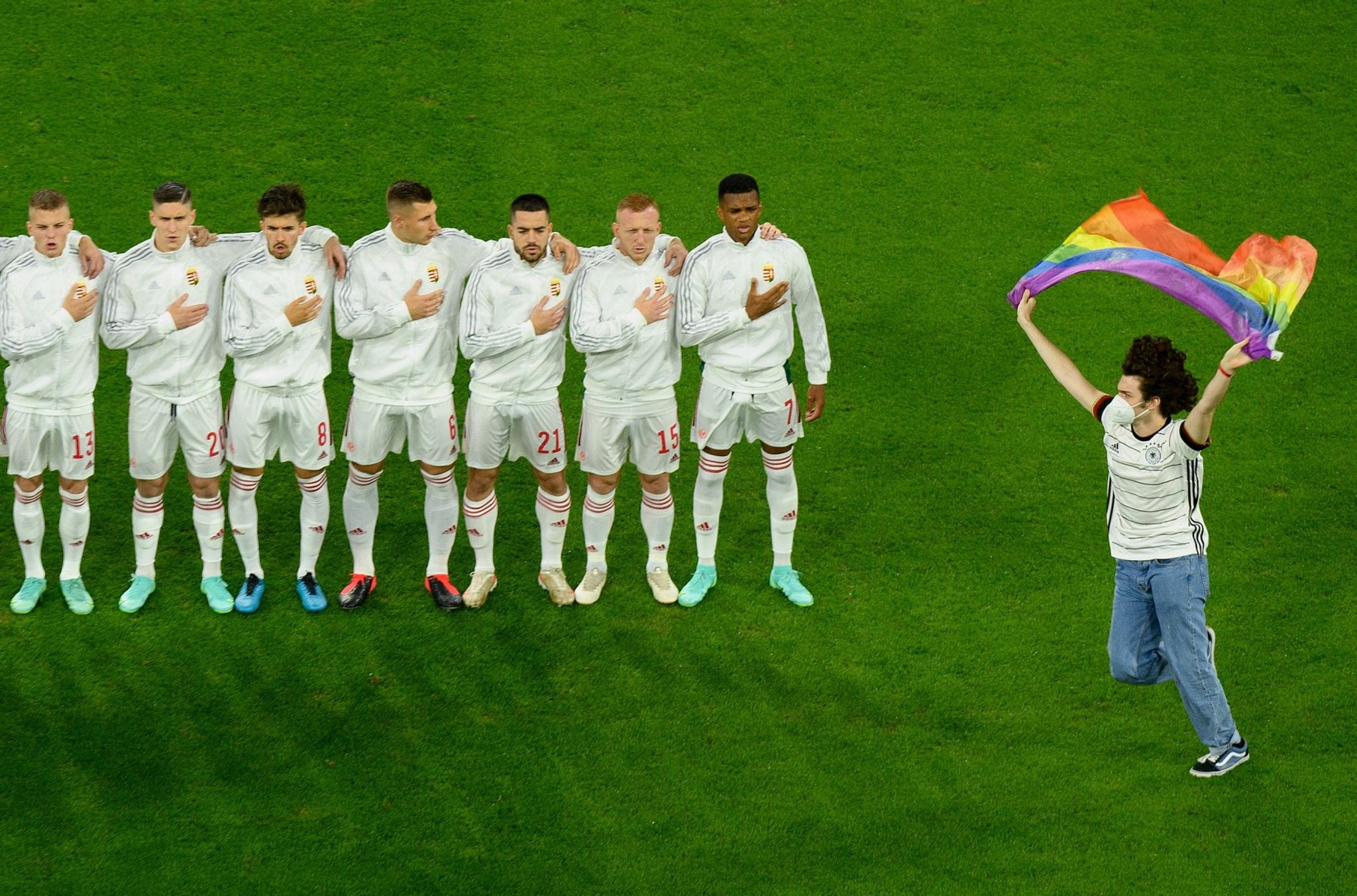 A fan runs on to the pitch waving a rainbow flag in front of Hungary's footballers