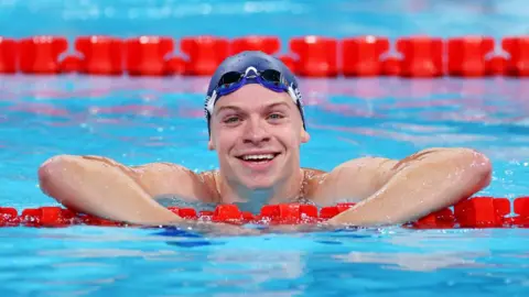 Getty Images Léon Marchand smiles to the camera from the pool