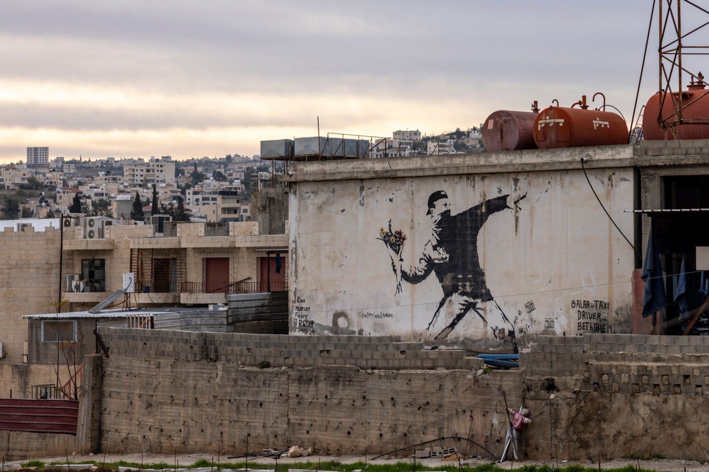 A Banksy mural of a young man with a bandana covering his face throwing a bouquet of flowers