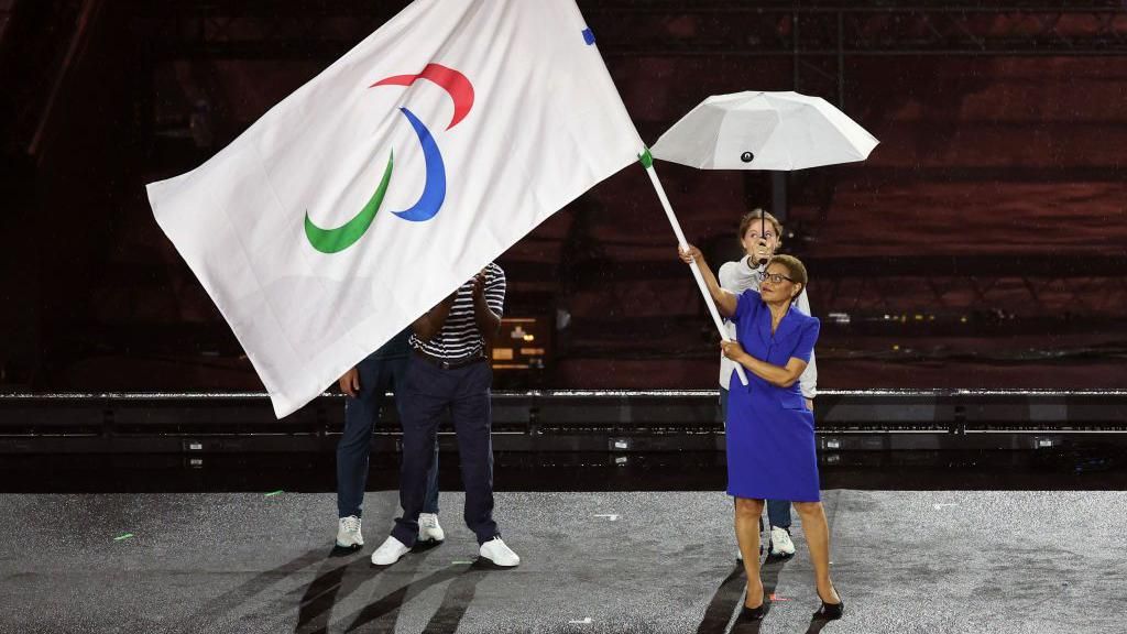 Los Angeles mayor Karen Bass sheltered under an umbrella as she waves the Paralympic flag 