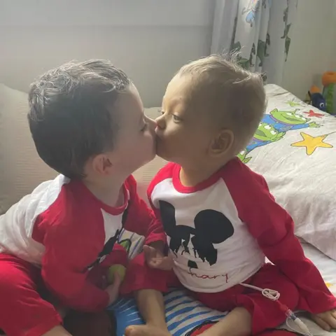 Bradford family Reuben and Zachary give each other a kiss - they are both wearing red Mickey Mouse pyjamas