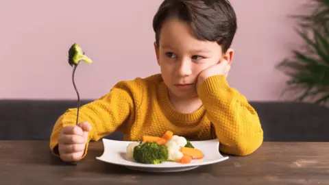 Getty Images Young boy looking skeptically at vegetables on his plate 