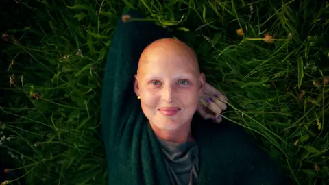 BBC/October Films/Neil Bonner Kris Hallenga lies on her back on the grass. She is resting her head on her arm. Kris is wearing a green top and is smiling. 