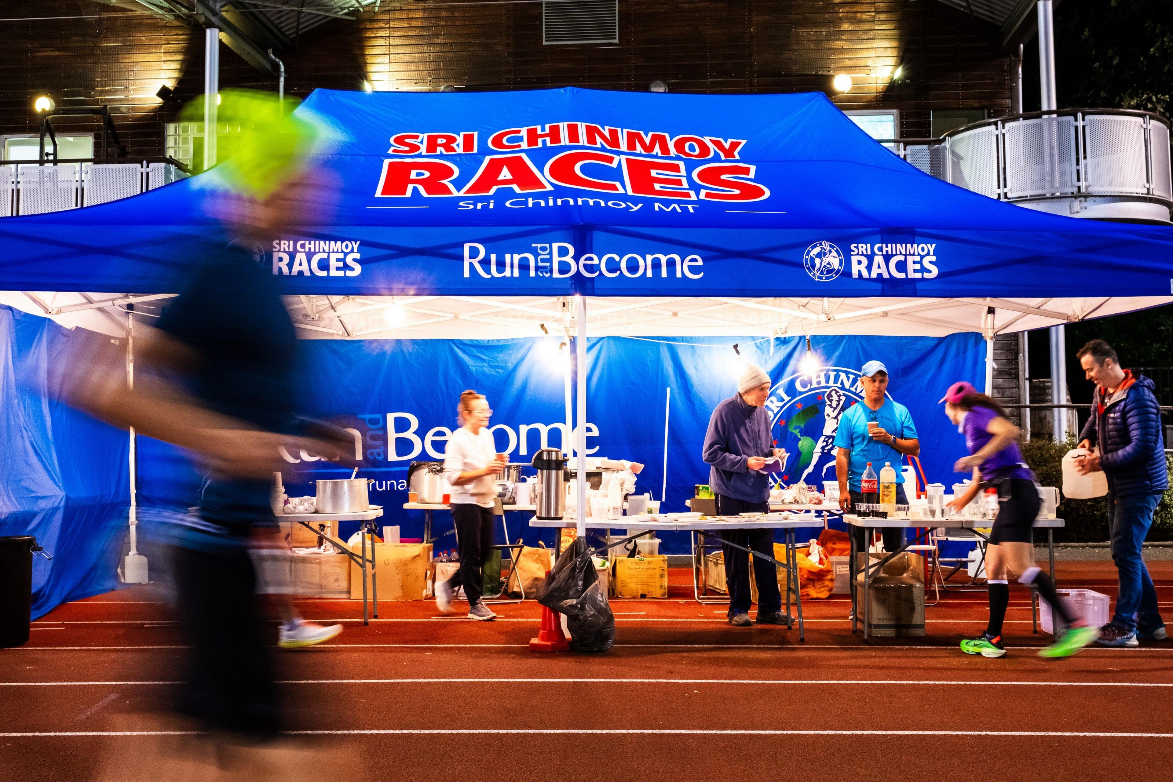 A runner takes food from an aid station as another runs past at the Sri Chinmoy 24hr Track Race in Battersea