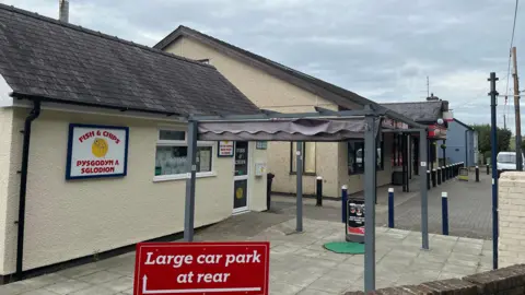 The exterior of buildings in Morfa Bychan, with a fish and chips sign and a sign for the car park