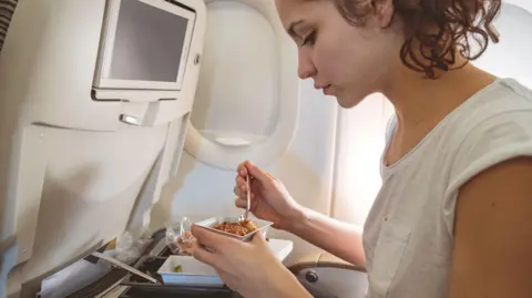 Getty Images A woman eating from a carton on a plane