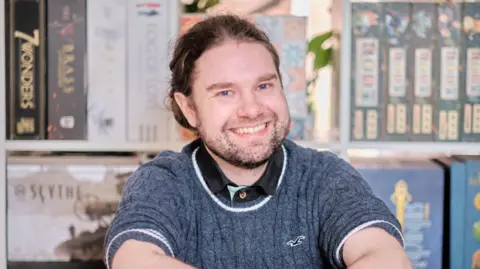 HANDOUT Kari, who has long brown hair tied back and is wearing a grey knitted jumper, smiles 