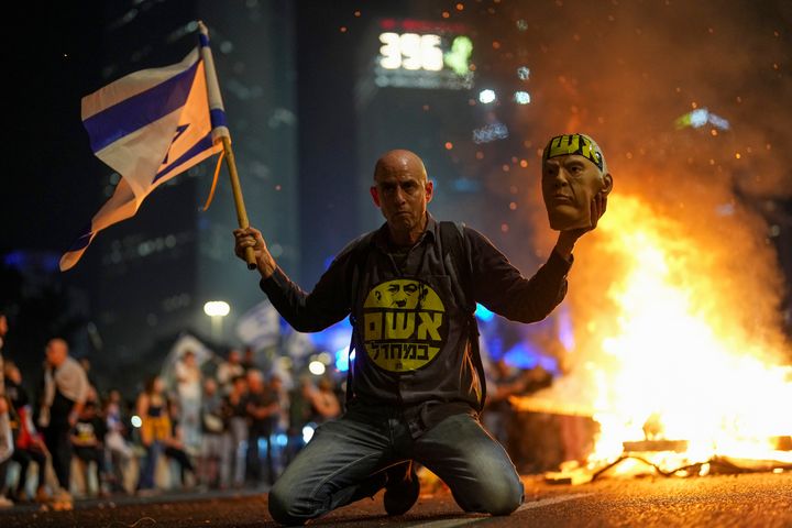 A protester holds an Israeli flag as Israelis light a bonfire during a protest after Prime Minister Benjamin Netanyahu has dismissed his defense minister Yoav Gallant in a surprise announcement in Tel Aviv, Israel, Tuesday, Nov. 5, 2024. (AP Photo/Francisco Seco)