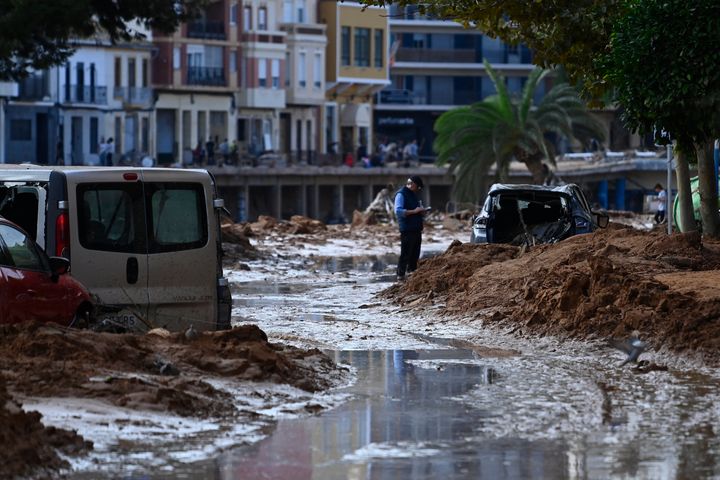 A man stands next to the wreckage of a car in a street covered in debris and mud on October 31, 2024 after flash floods affected Paiporta, in Valencia, eastern Spain. (Photo by JOSE JORDAN/AFP via Getty Images)