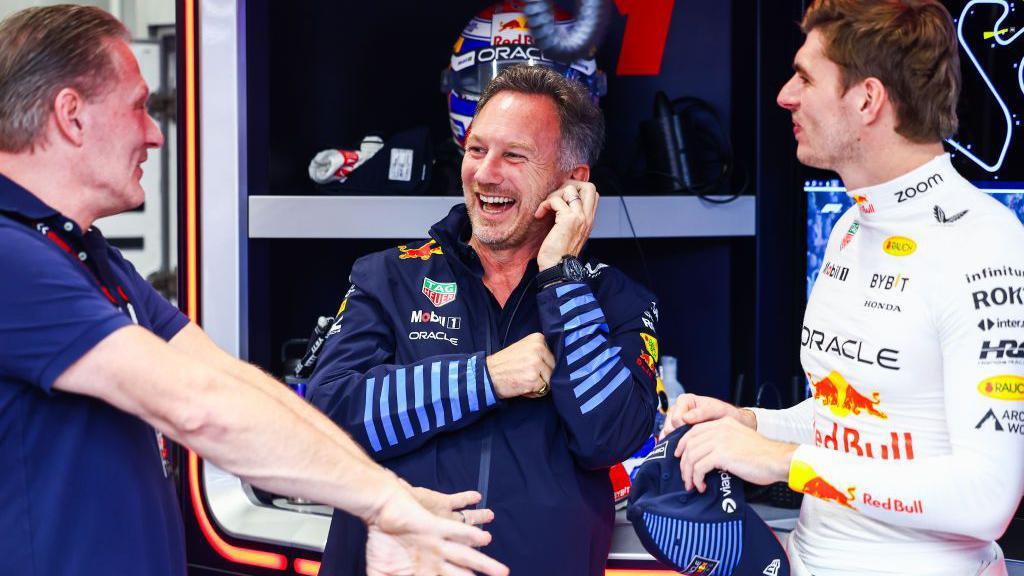 Red Bull team boss Christian Horner smiles as he listens to Jos Verstappen speak with Max Verstappen stood to the right of them both