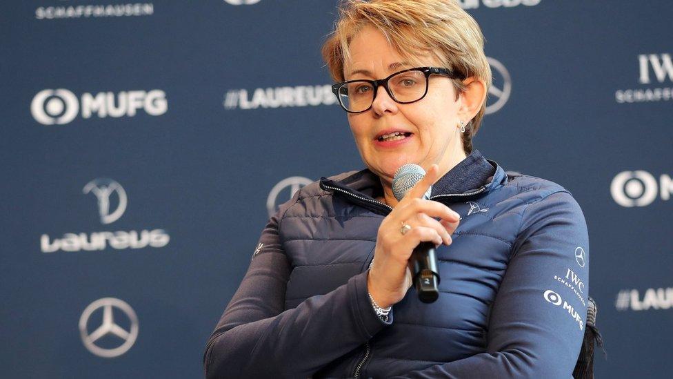 Baroness Tanni Grey-Thompson wears black glasses and a blue anorak, and is holding a microphone