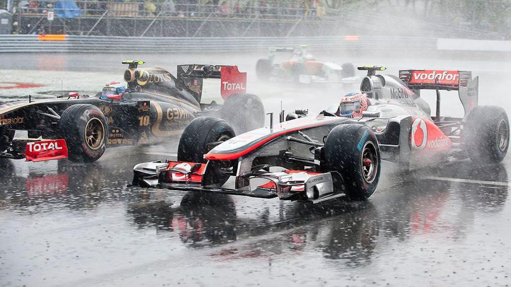 Jenson Button passes the Lotus of Vitaly Petrov as rain hammers on to the circuit during the 2011 Canadian Grand Prix