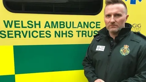 Jason Killens, chief of the Welsh Ambulance service, in uniform standing by one of his vehicles 