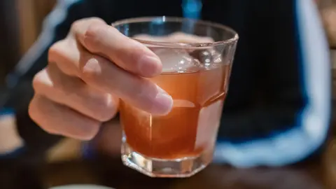 Getty Images A close-up of an anonymous man holding a tumbler filled with dark alcohol and ice