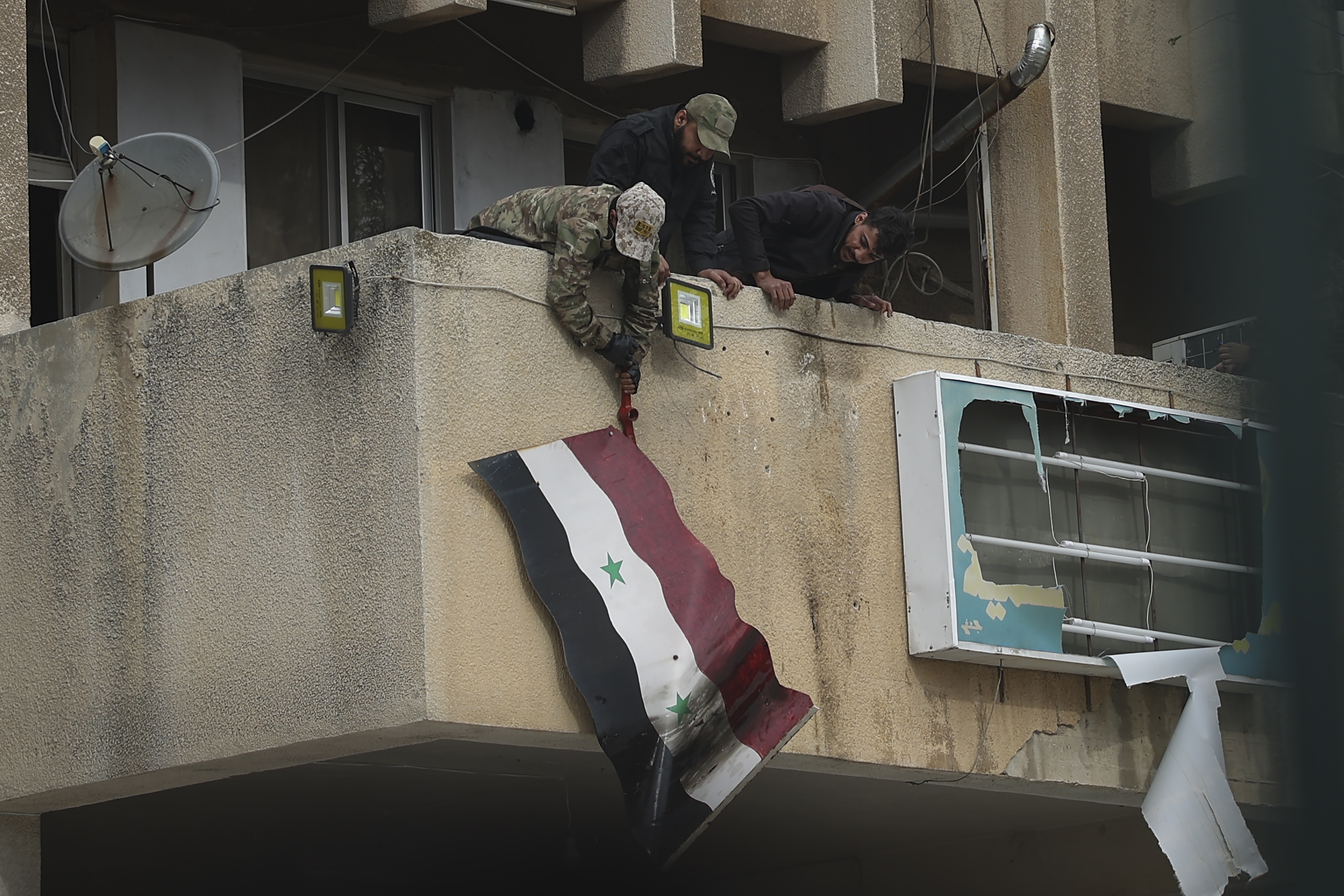 Syrian opposition fighters remove a government Syrian flag from an official building in Salamiyah, east of Hama, Syria Syria, Saturday Dec. 7, 2024. (AP Photo/Ghaith Alsayed)