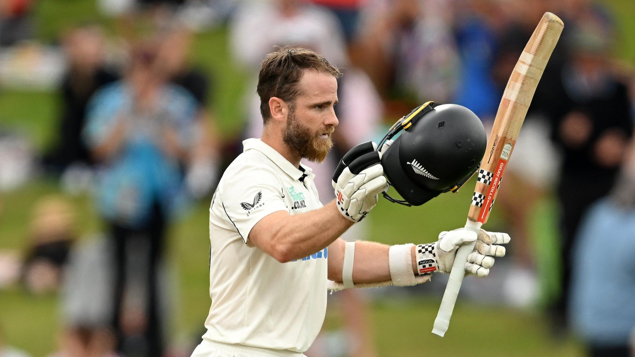 New Zealand batter Kane Williamson raises his bat and helmet after hitting a century