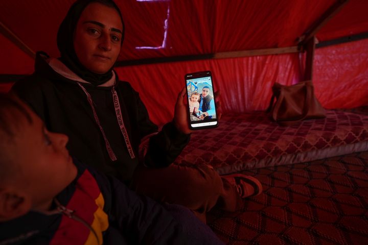 Sitting next to her son Wael (L), Reem Ajour shows a picture of her missing daughter, Masaa, and her missing husband, Talal, on her phone in a camp outside Zuweida, Gaza Strip, Nov. 20, 2024.