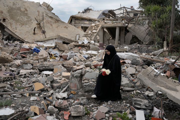 A Lebanese woman holds a bouquet of flowers as she sits on the rubble of a house destroyed by the Israeli forces, in the Aita al-Shaab village that sits on the Israeli-Lebanese border, on Sunday, Jan. 26, 2025.