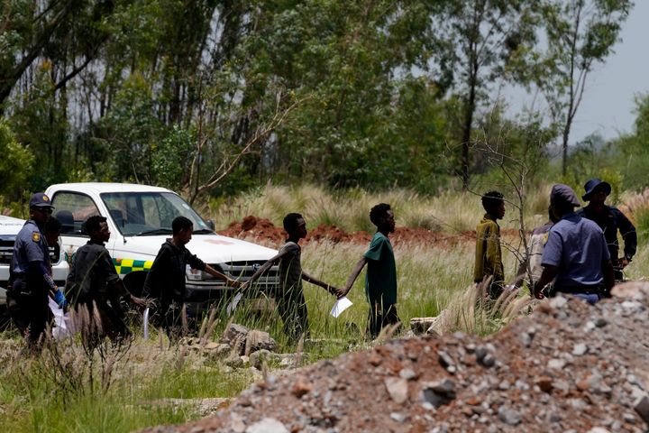 Miners are escorted by police officers after being rescued from the abandoned gold mine on Tuesday.