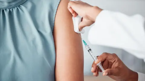 Getty Woman in a blue silk sleeveless job receiving an injection from a medical professional