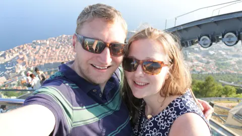 Family handout Jamie and Kate Scott pictured in a selfie while on holiday. They both wear sunglasses and the shot shows them up high with a view of seaside town behind them below.