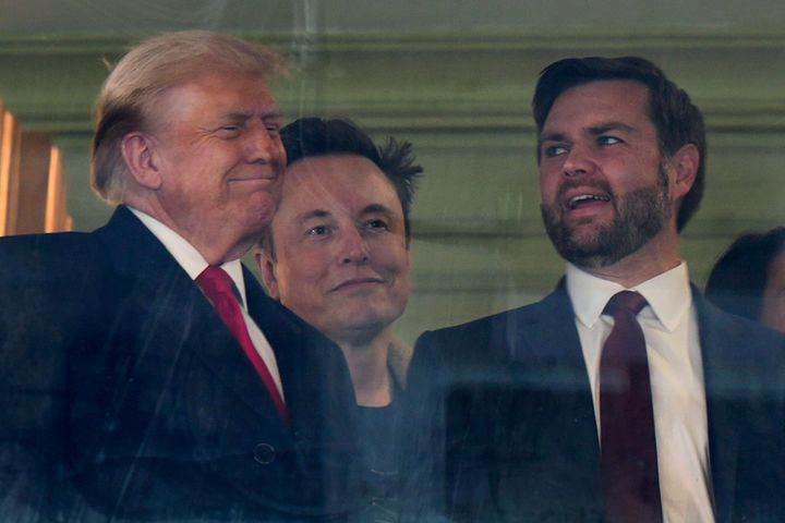 In this picture taken through a window, President-elect Donald Trump, Trump's pick for the planned Department of Government Efficiency Elon Musk and Vice President-elect JD Vance attend the NCAA college football game between Army and Navy at Northwest Stadium in Landover, Md., Saturday, Dec. 14, 2024. (AP Photo/Stephanie Scarbrough)