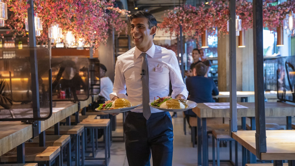 Former Chancellor Rishi Sunak carries two plates of food in a branch of Wagamama's to promote the "Eat Out To Help Out" scheme he launched during Covid.