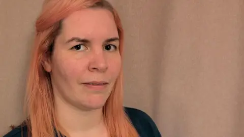 Anna Malnutt Woman in her thirties with long strawberry blonde hair and a pensive look on her face