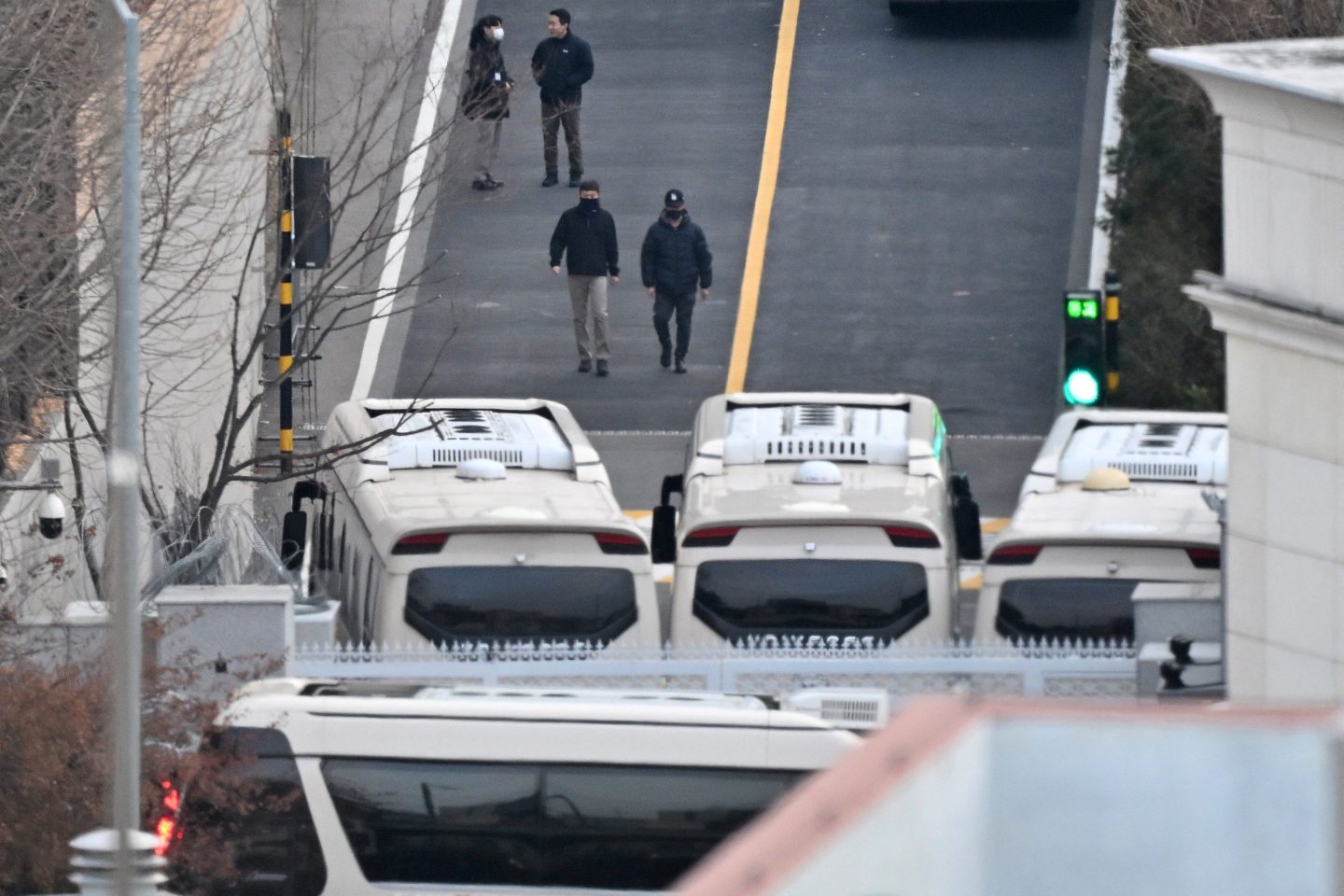 Security personnel walk on a road lined with buses blocking the entrance gate of the presidential residence to protect impeached South Korean president Yoon Suk Yeol from a possible second arrest attempt by the Corruption Investigation Office for High-ranking Officials (CIO), in Seoul on Jan. 8, 2025. 