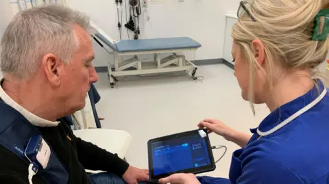 NEWCASTLE HOSPITALS Kevin is with a nurse at hospital as the new system is re-programmed and switched on. They are both looking at a computer screen which is wired to his chest. 