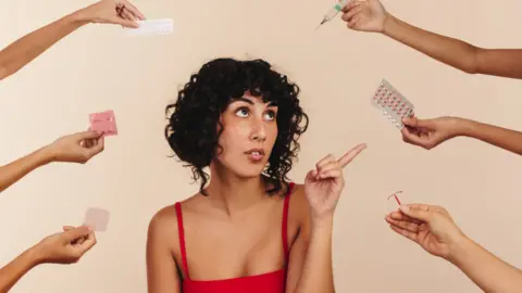 Getty Images A woman sits looking at different contraceptive choices, including pills and condoms