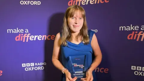 Mikayla Beames, standing in front of a purple BBC Make a Difference background, and holding an award.