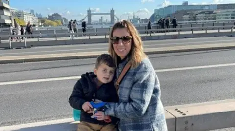 Moorfields Hospital Jace and his mum DJ having their photo taken in London on a sunny day with blue skies, with Tower Bridge in the background